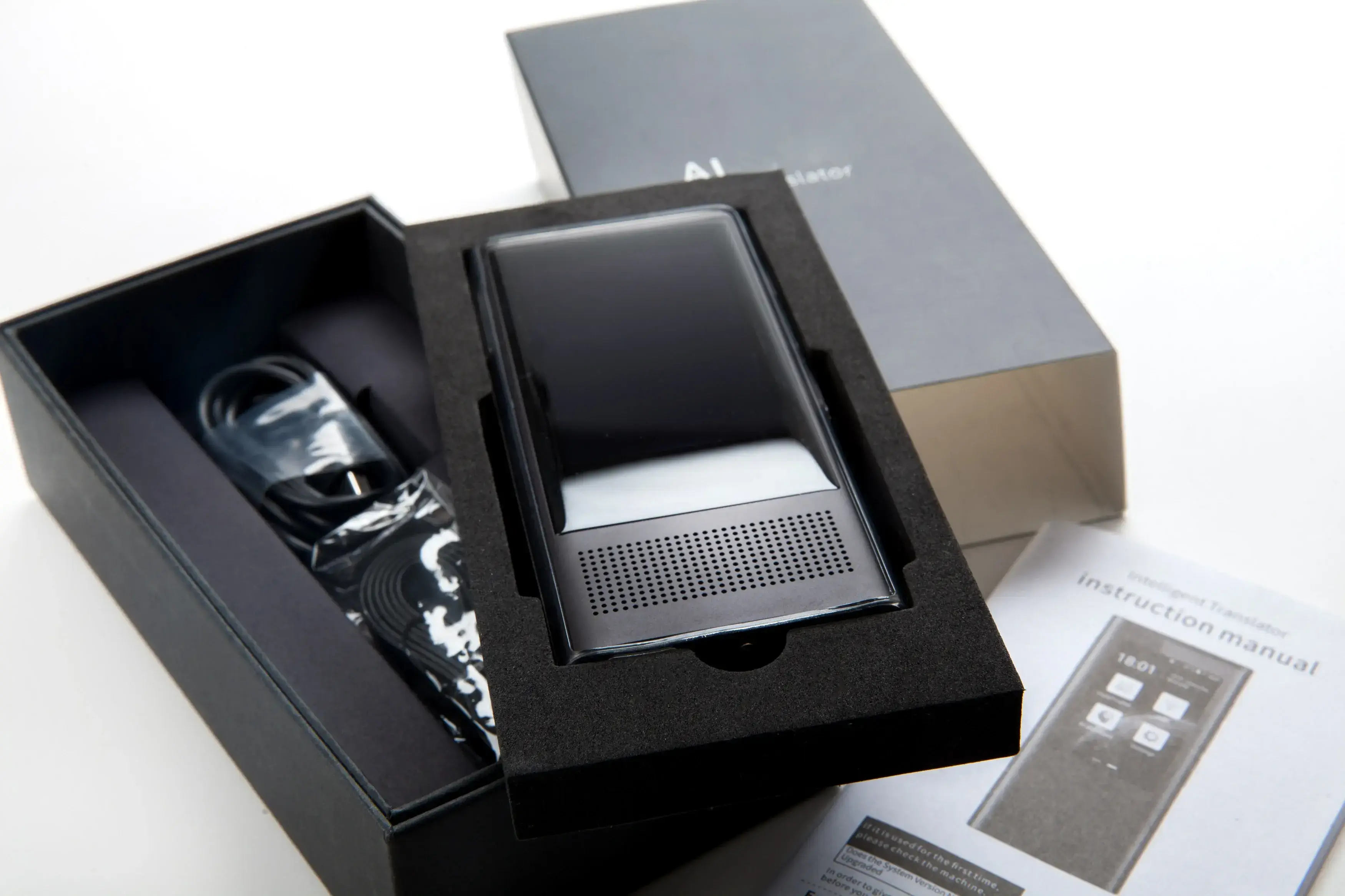 KI-Gesprächs- und Bild-Übersetzungsgerät in einer offenen schwarzen Box und einem Buch mit Anweisungen.